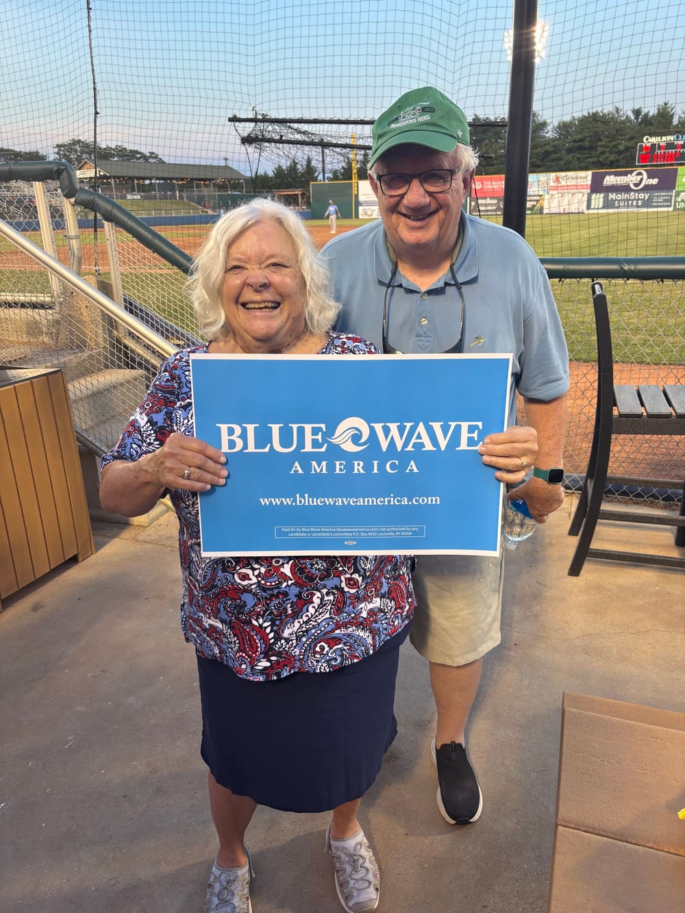 Supporters holding a Blue Wave America sign at a ballpark.